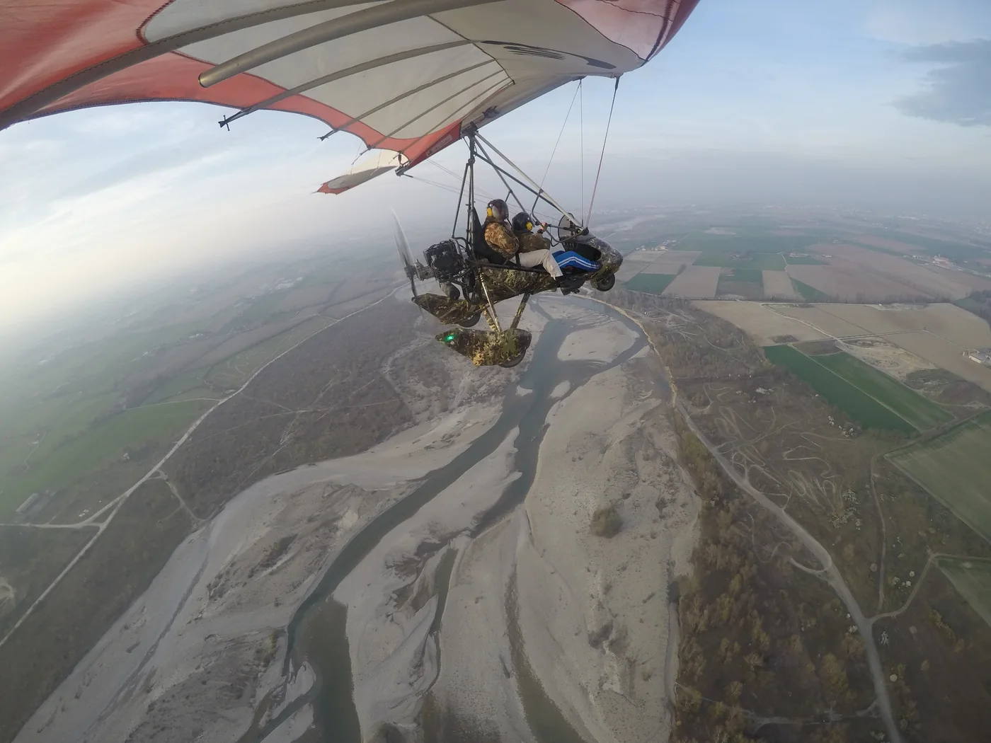 Deltaplano a motore biposto in volo sopra un fiume e la pianura